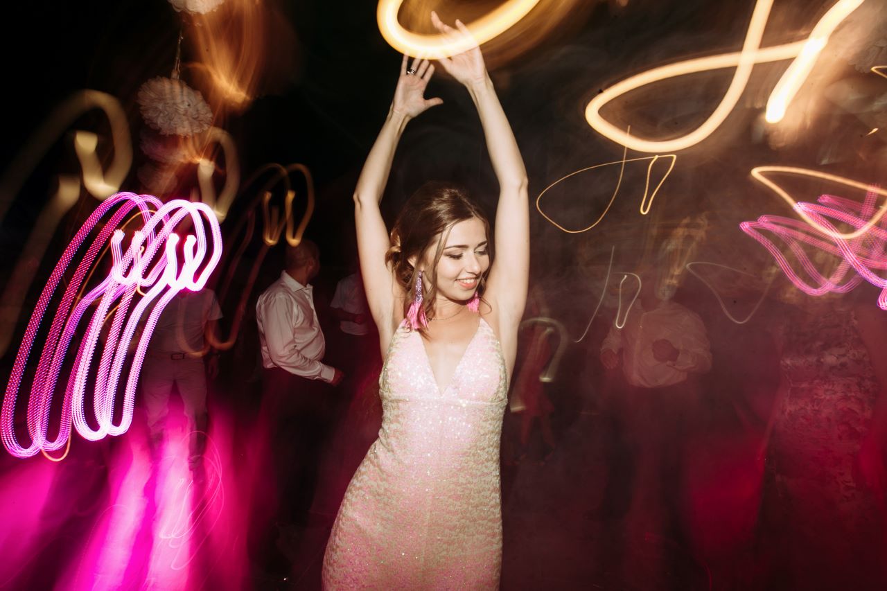 bride dancing in white dress with large neon lights surrounding her